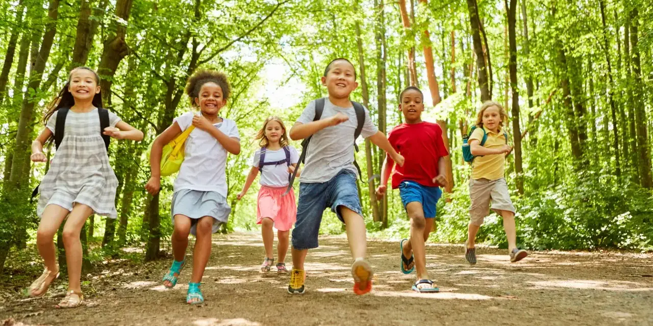 Des enfants joyeux, des supernova juniors, courent sur un sentier forestier ensoleillé, pleins d'énergie.
