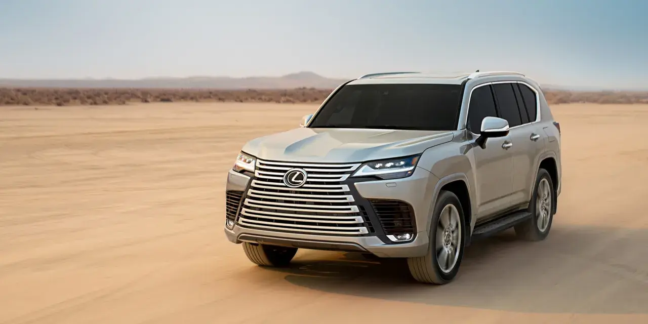 Srebrny Lexus LX 600 przemierza pustynię, zostawiając ślady na piasku.
