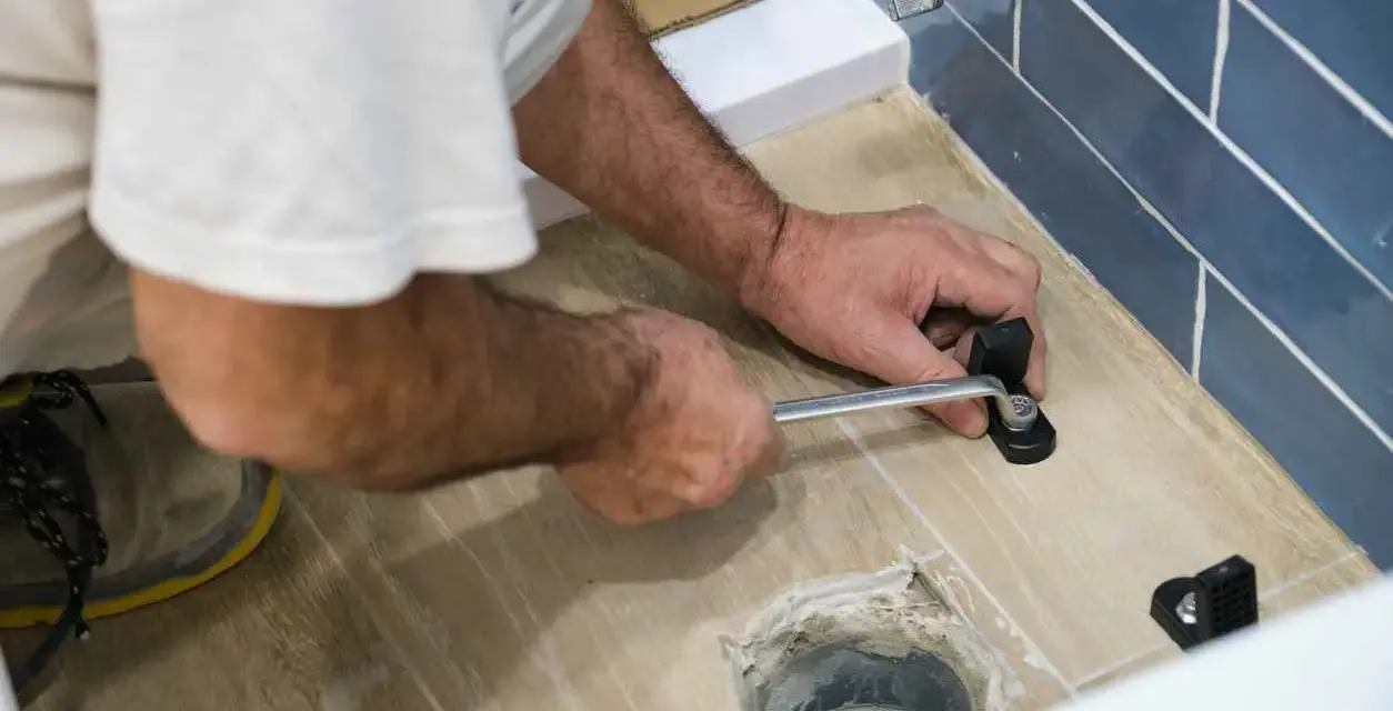 A person uses a wrench to tighten a toilet flange bolt, demonstrating how to replace a toilet flange.