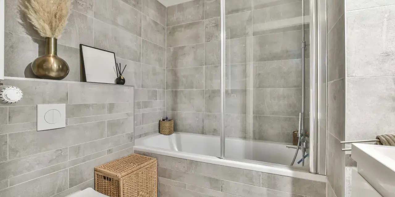 Salle de bain entierement carrelée de gris, avec baignoire, douche, lavabo et WC. Un panier en osier et des herbes séchées apportent une touche naturelle.