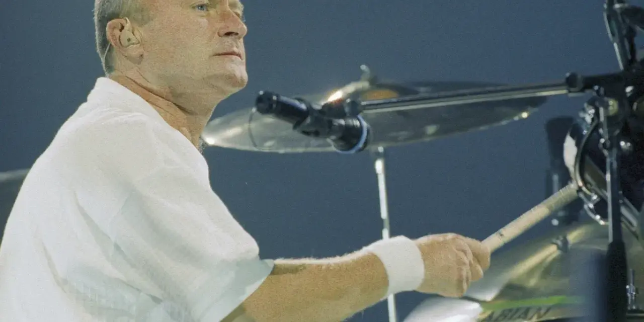 Phil Collins, w białej koszuli, gra na perkusji. Legendarny muzyk, znany z zespołu Genesis.