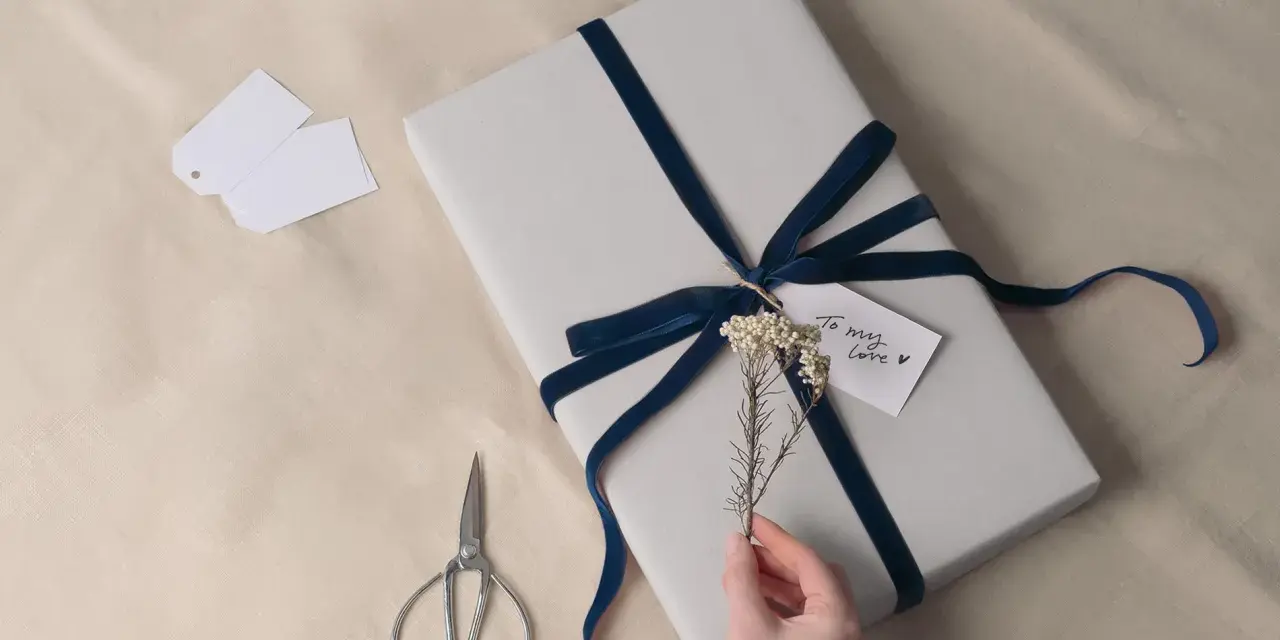 Prezent na 8 rocznicę ślubu, owinięty w szary papier i ozdobiony granatową aksamitną wstążką. Drobna gałązka i karteczka "To my love" dodają uroku.