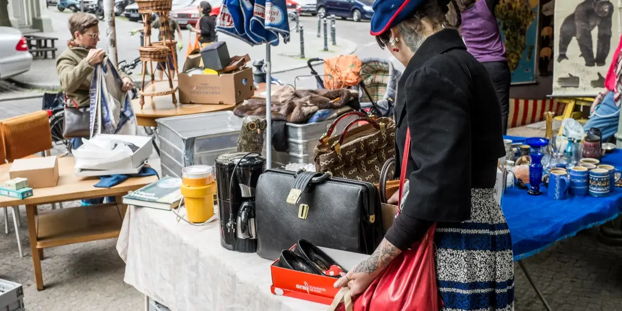 Frau mit Tätowierungen auf dem Arm sucht auf einem antik flohmarkt nach Schätzen. Sie hält eine rote Tasche.
