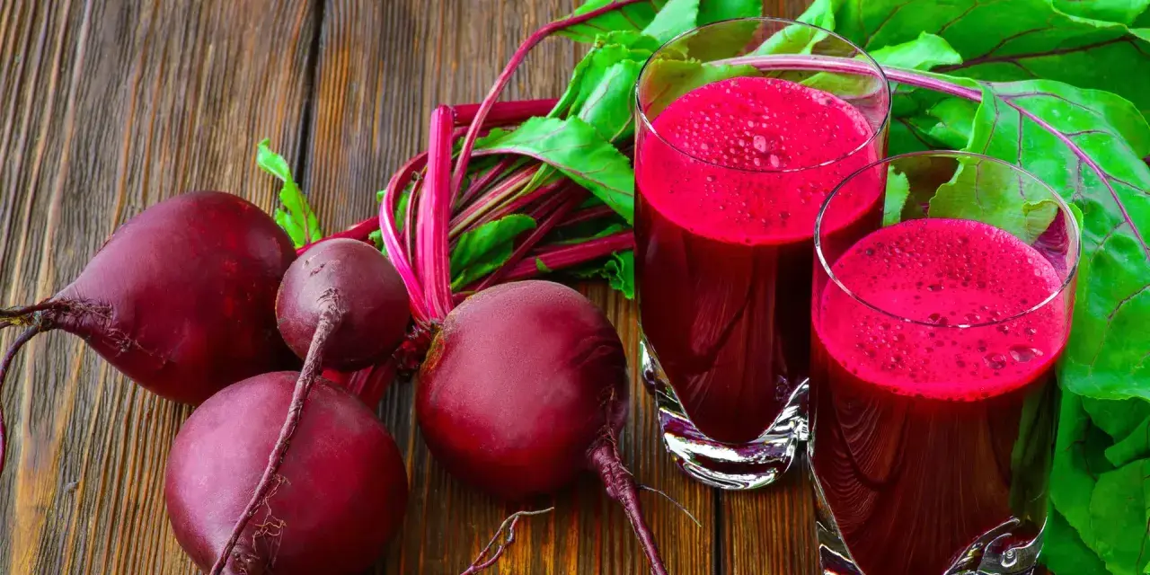 Frische rote Bete und zwei Gläser mit leuchtend rotem Rote-Bete-Saft stehen auf einem Holztisch.