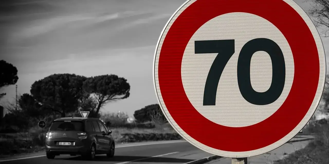 Segnale 226: limite di velocità 70. Un'auto viaggia su una strada panoramica.