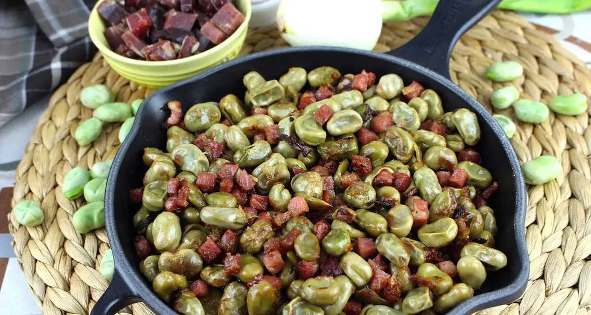 Habas tiernas salteadas con trocitos de jamón en una sartén de hierro fundido, un plato tradicional lleno de sabor.