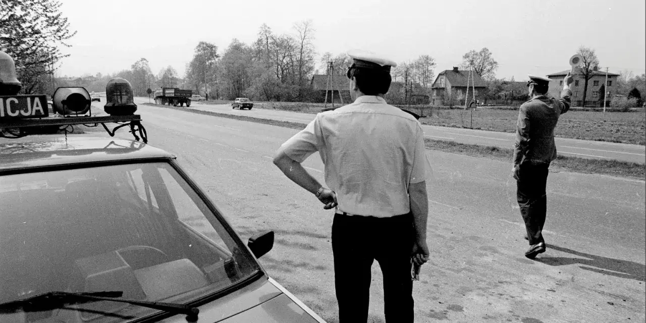 Policjanci na gierkówce kontrolują ruch. Jeden z nich stoi przy radiowozie, drugi kieruje ruchem.