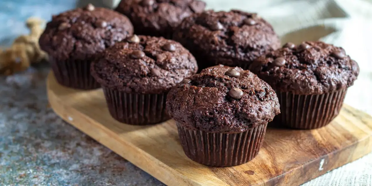 Fem saftiga chokladmuffins med chokladknappar på en träbricka. Perfekt för ett chokladmuffins recept.