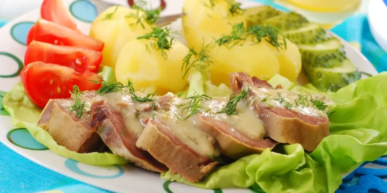 Pokrojone ozory wieprzowe w sosie, podane z ziemniakami, pomidorami i ogórkiem kiszonym.