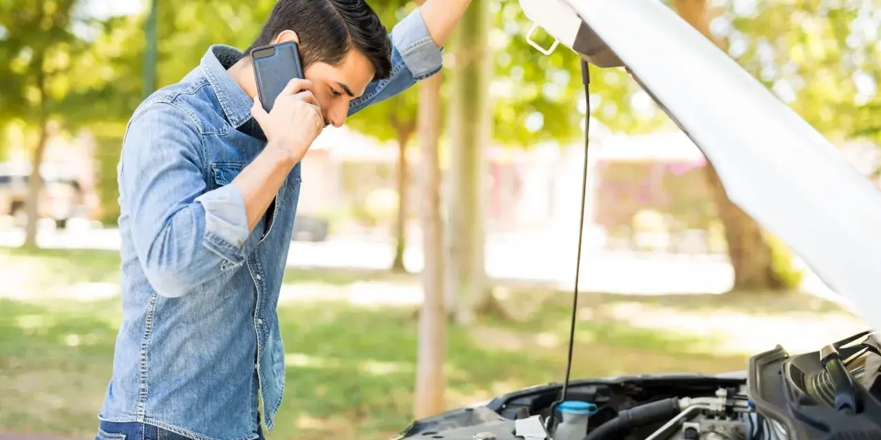 Mann telefoniert neben offenem Motorraum. Was ist beim Abschleppen zu beachten bei PKW Defekt?