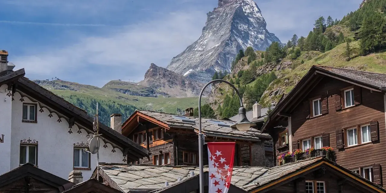 Tradycyjna winieta szwajcaria: drewniane domy z kamiennymi dachami i majestatyczny Matterhorn w tle.