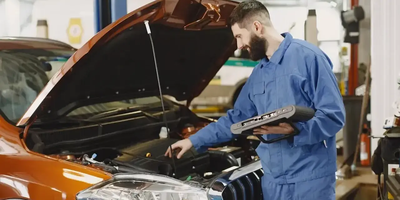Mechanik z komputerem diagnostycznym sprawdza silnik pomarańczowego auta. Zastanawiasz się, ile trwa wymiana oleju?