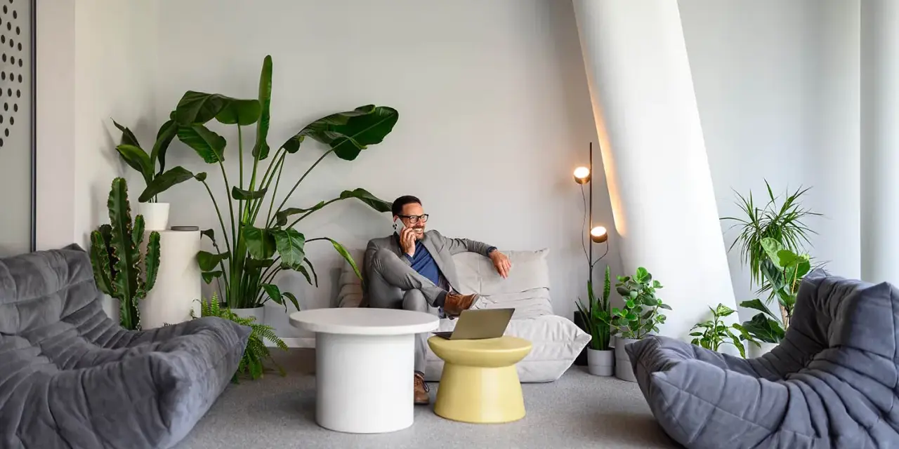 Un homme d'affaires au téléphone dans un coin salon moderne avec des plantes, une idée pour optimiser petit espace.