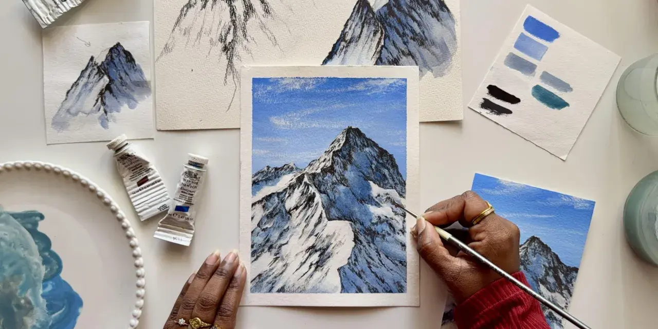 Une main peint une peinture montagne facile, avec des tubes de peinture et des nuanciers bleus à proximité.