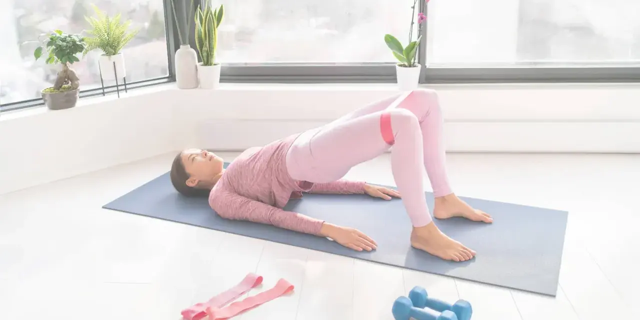 Femme faisant un pont avec une bande de résistance pour comment muscler les fessiers. Haltères et bandes roses à proximité.