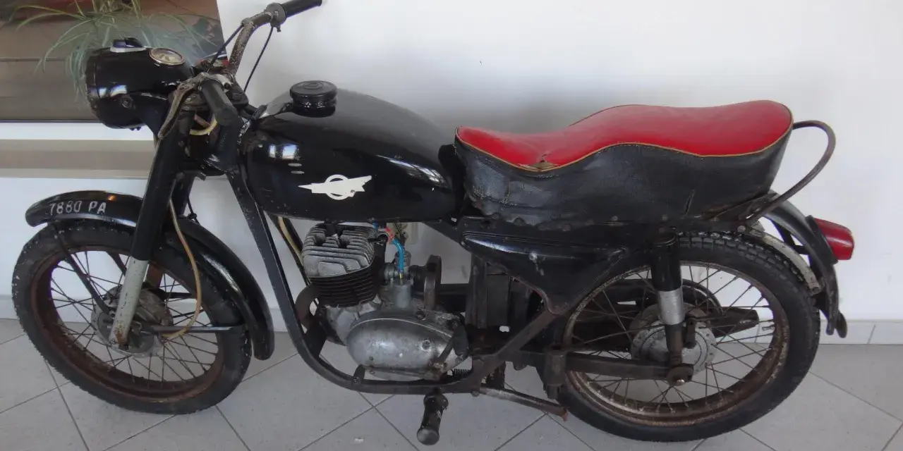 Czarny motocykl wsk 125 z czerwoną kanapą, stojący na szarej podłodze.
