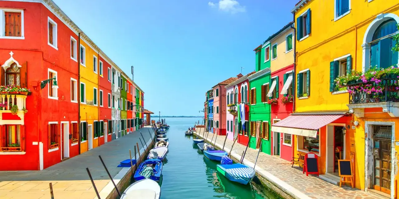 Coloratissima isola a Venezia, con case vivaci affacciate su un canale pieno di barche.