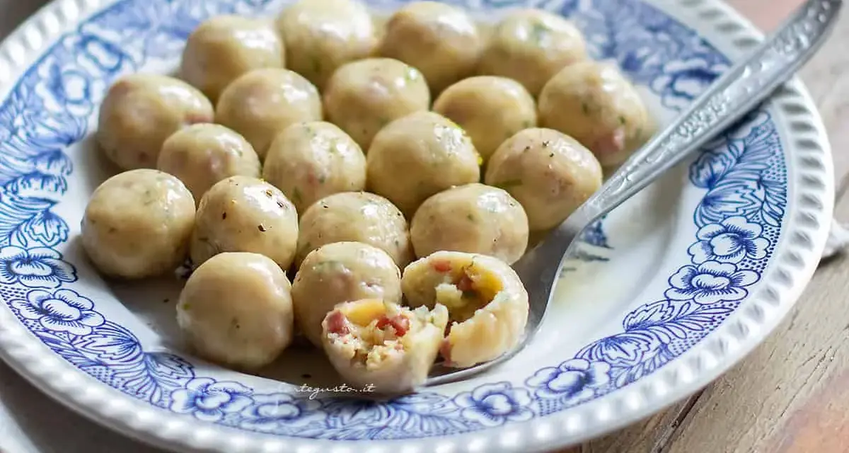 Gnocchi di pane saporiti, serviti su un piatto decorato. Uno è tagliato a metà, rivelando un ripieno gustoso.