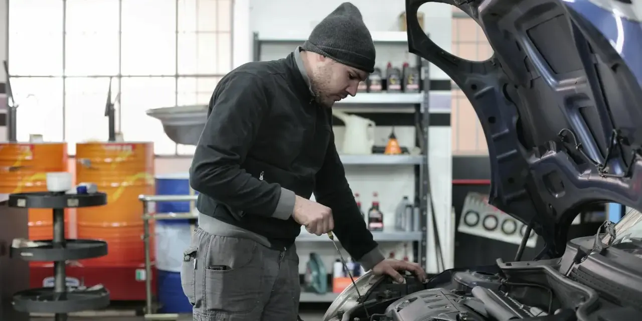 Mechanik w czapce z daszkiem sprawdza silnik. Zastanawiasz się, ile zarabia mechanik? Praca wymaga precyzji i wiedzy.
