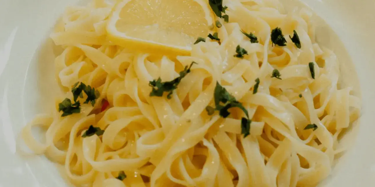 En portion krämig citronpasta med färsk persilja och en citronskiva. Perfekt till ett glas vitt vin.