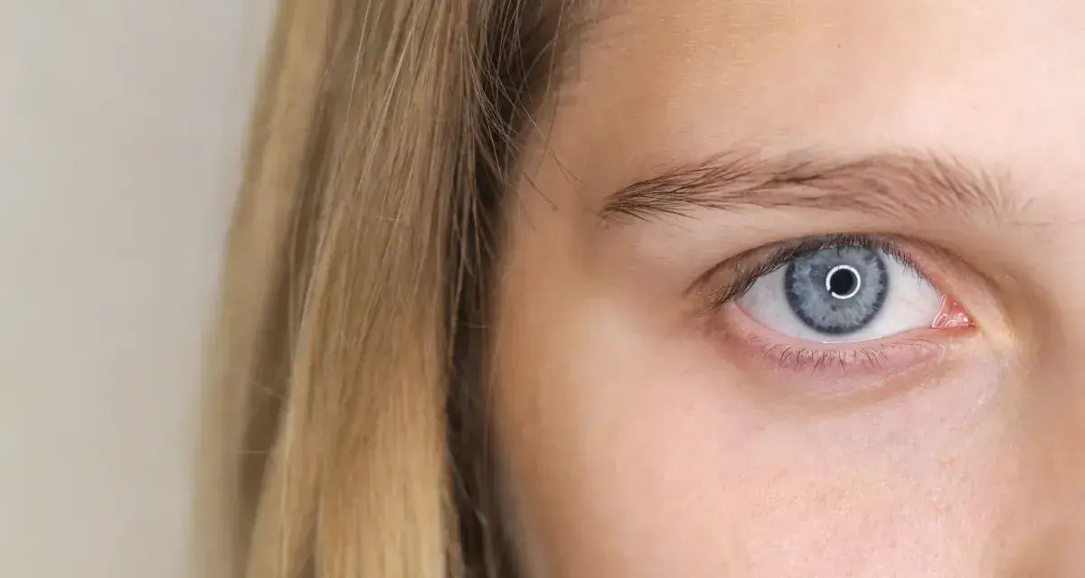 Zbliżenie na niebieskie oko dziewczyny z blond włosami. Powiększone źrenice sugerują zaciekawienie lub zaskoczenie.