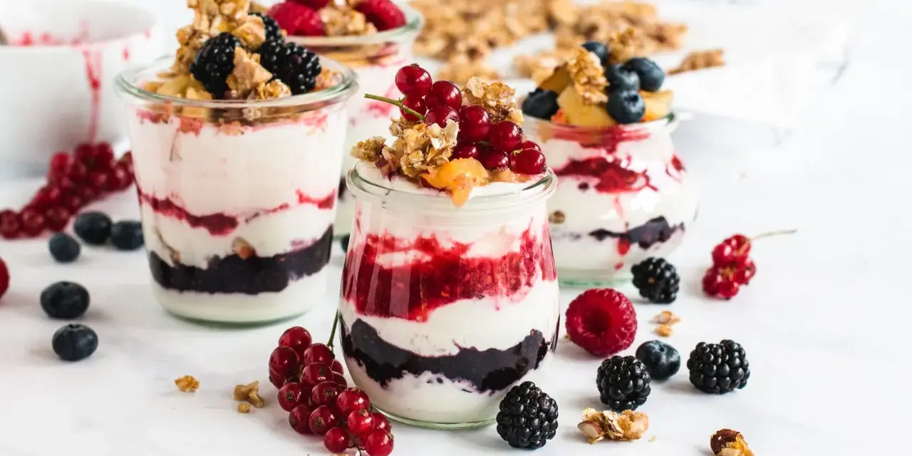 Leckeres Dessert mit Beeren und Joghurt in Gläsern geschichtet, garniert mit Granola und frischen Früchten.