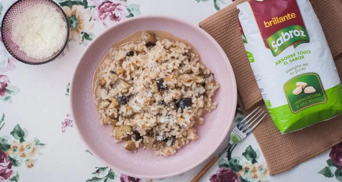 Arroz meloso con berenjenas en plato rosa, acompañado de queso rallado y bolsa de arroz Sabroz.