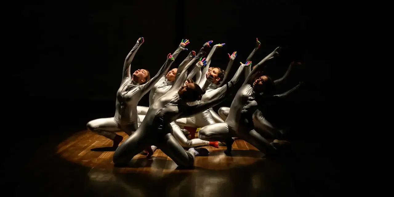 Un groupe de danseurs en costumes argentés, mains levées, dans un photo spectacle captivant.