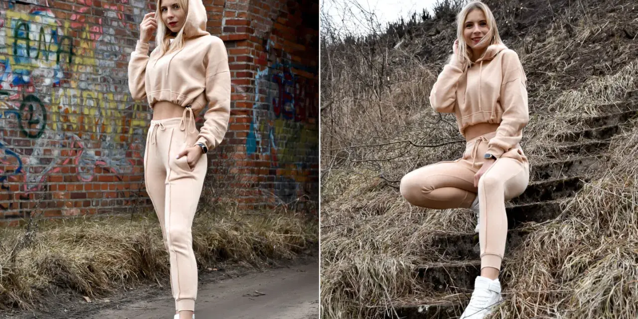 Dresy damskie szerokie w beżowym kolorze, idealne na co dzień. Modelka prezentuje je na tle ceglanej ściany i schodów.