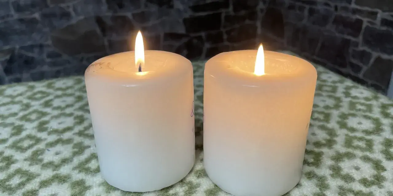 Two white candles glow softly, their flames flickering. This peaceful scene evokes the second Sunday of Advent theme of hope and preparation.