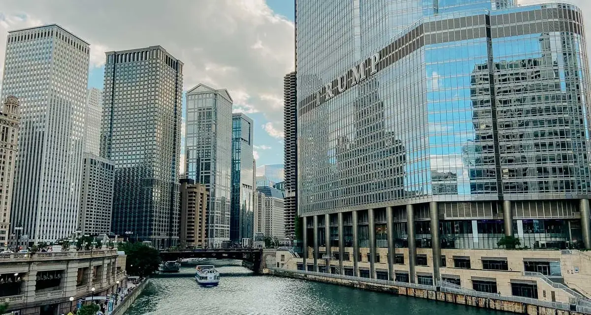 Chicago's iconic skyline along the river, with the Trump Tower reflecting the clouds. A boat glides by, making you wonder, is Chicago worth visiting?