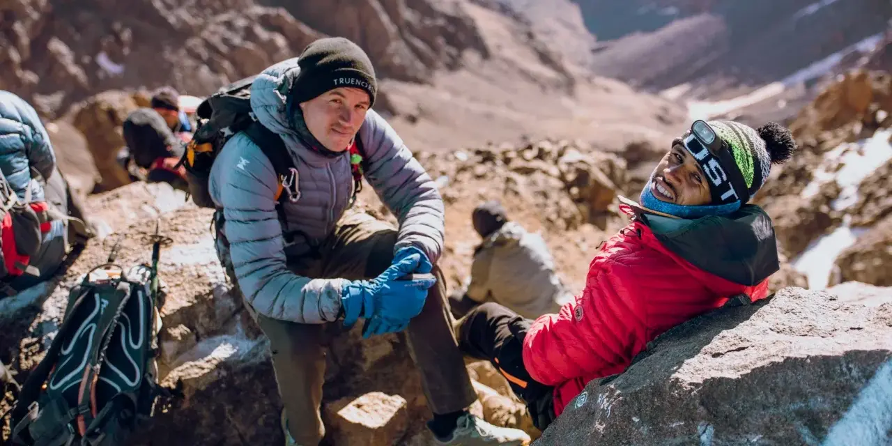 Uśmiechnięci alpiniści podczas wyprawy na Toubkal. W tle skaliste zbocza górskie.