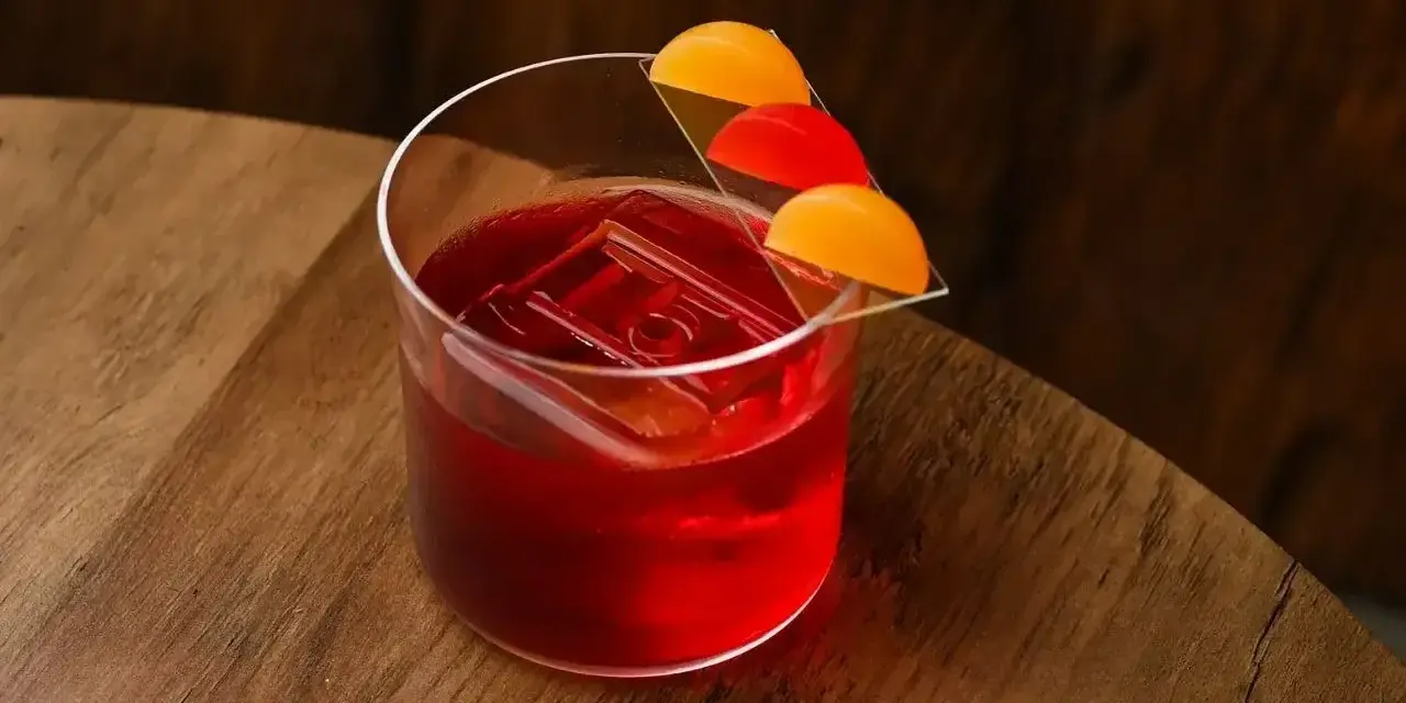 Klasyczny negroni przepis: czerwony koktajl z lodem i pomarańczową dekoracją na drewnianym blacie.