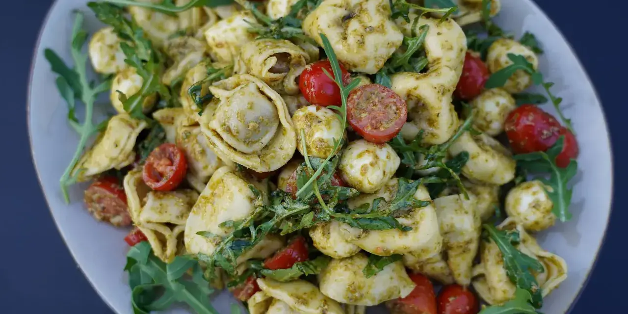 Ein köstlicher Tortellini-Salat mit Pesto, Kirschtomaten und Mozzarella-Kugeln, garniert mit Rucola.