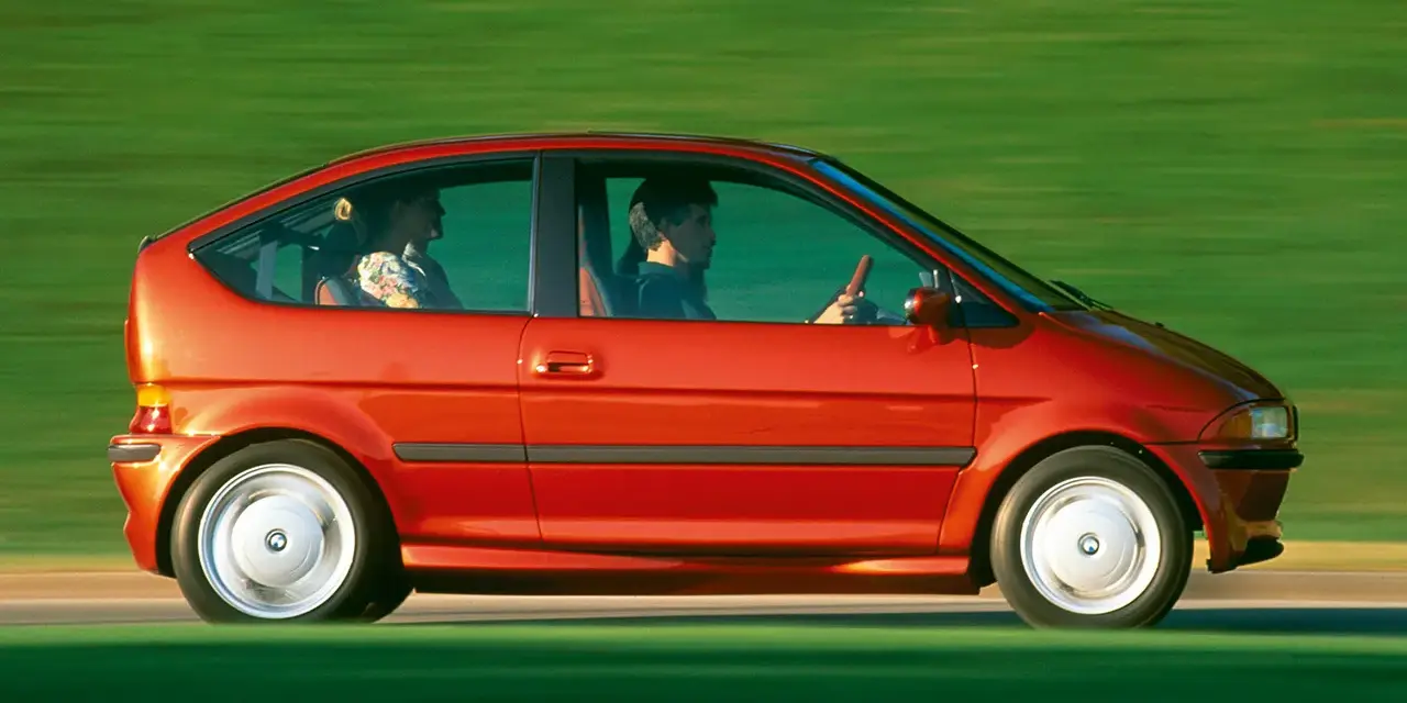 Czerwony samochód elektryczny BMW E1 z lat 90. jadący po zielonym tle.