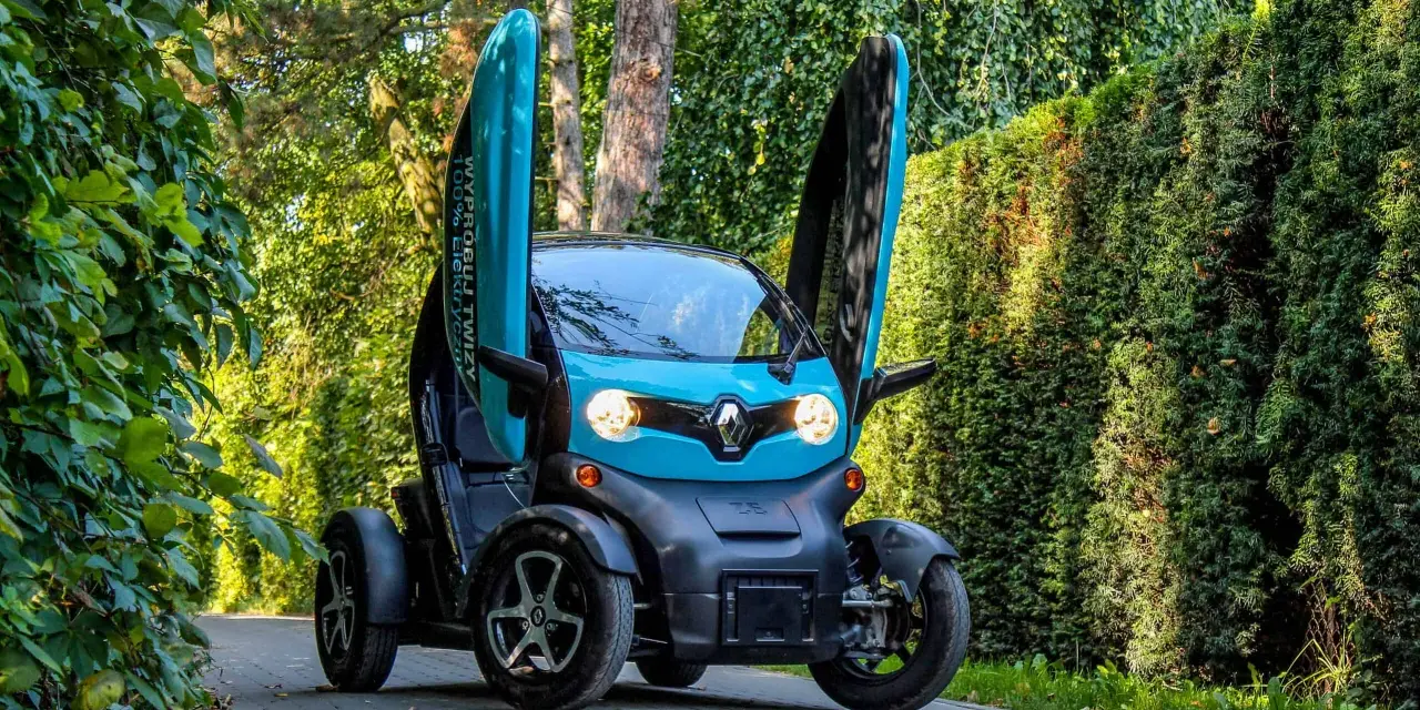 Niebieski Renault Twizy z otwartymi drzwiami stoi na ścieżce wśród zieleni.