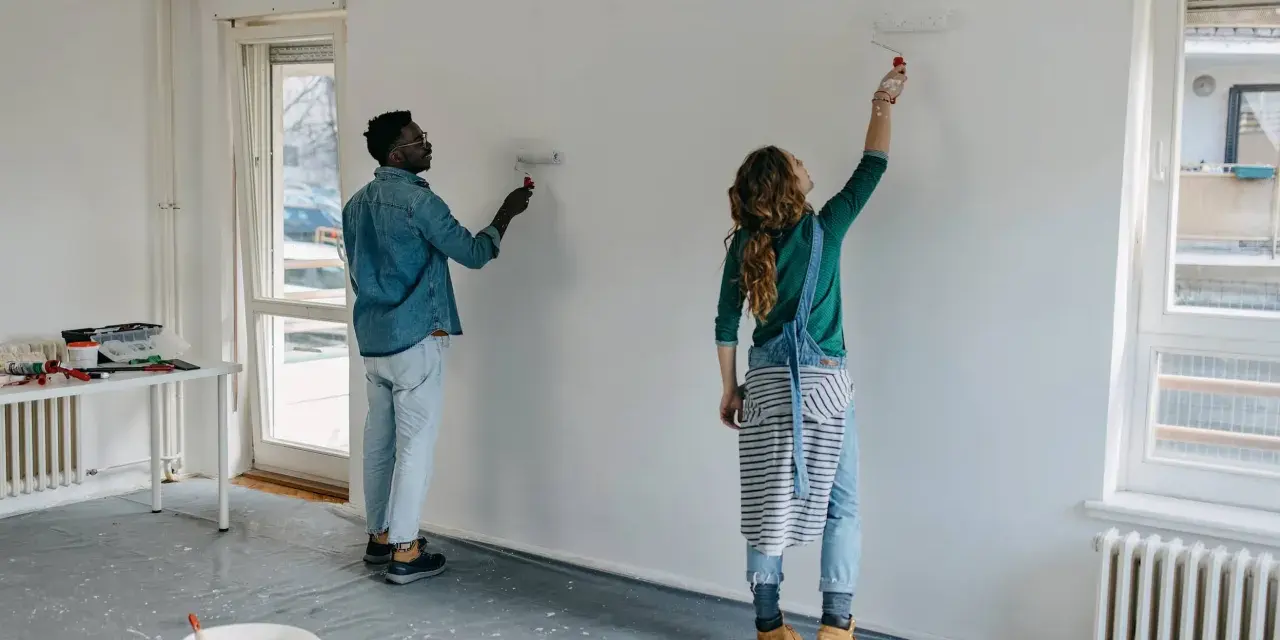 Pareja pintando una pared blanca, renovando su hogar. El hombre y la mujer usan rodillos para pintar sobre lacado, transformando el espacio.