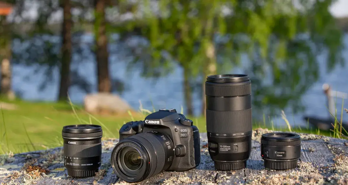 Aparat Canon EOS 90D z obiektywami 10-18mm, 70-300mm i 50mm na kamieniu nad jeziorem.