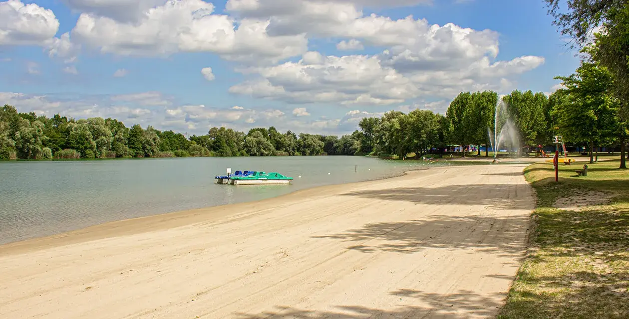 Sommerliche Idylle am Baggersee: Sandstrand, Tretboote und eine Fontäne laden zum Entspannen ein. Hier lässt sich das Leben in Karlsruhe genießen.