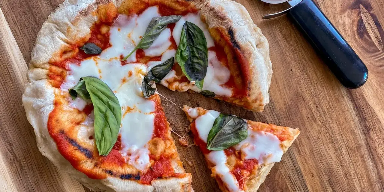 Pizza in padella appena sfornata, con pomodoro, mozzarella filante e basilico fresco, pronta per essere tagliata.