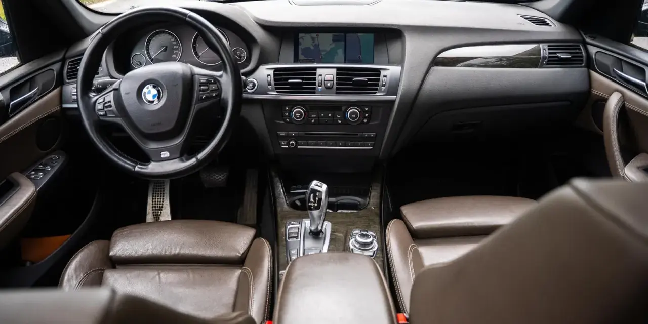 Wnętrze BMW X3 z brązową skórzaną tapicerką i drewnianymi wstawkami. Kierownica, deska rozdzielcza i nawigacja. Wiele osób szuka bmw x3 opinie, by poznać ten model.