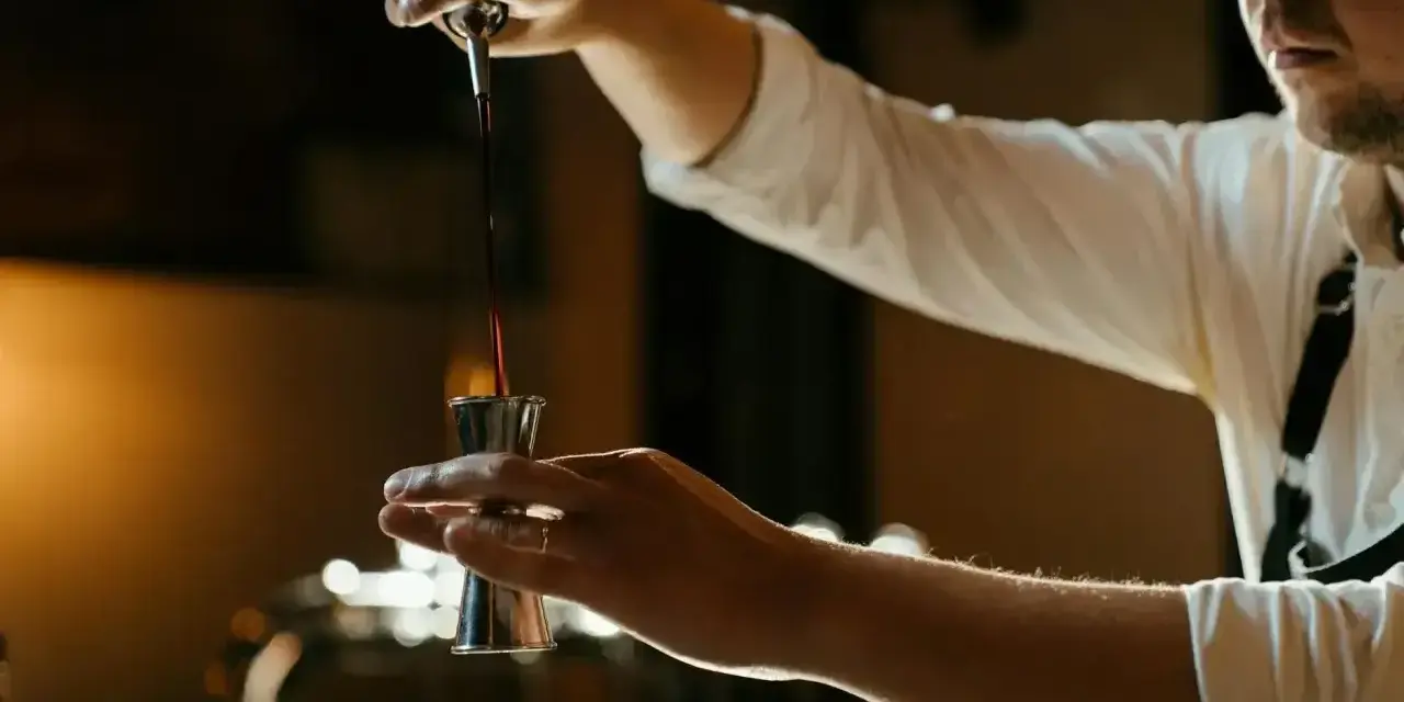 Barman nalewa ciemny płyn do jiggera, przygotowując drinka z Jägermeisterem i sokiem pomarańczowym.