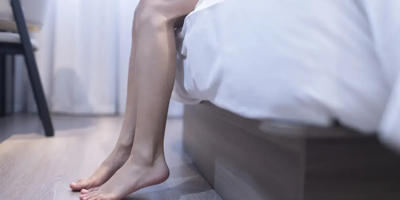 Kvinnans ben sitter på sängkanten, kanske plågade av myrkrypningar i benen under klimakteriet.