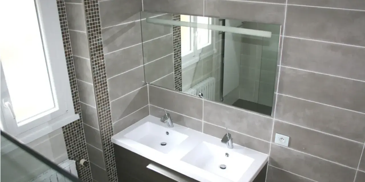 Salle de bain moderne avec double vasque. Le carrelage sol gris, posé au mur, crée une ambiance élégante.
