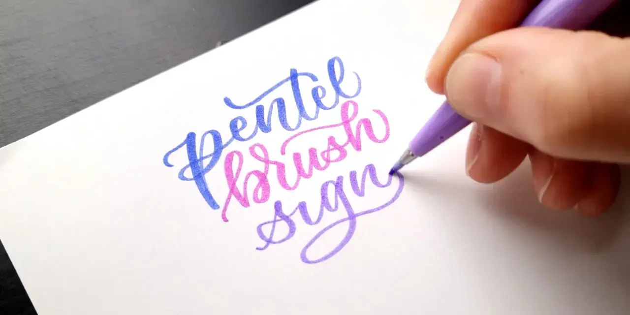 En hand skapar vacker brush lettering med en lila penna. Orden "Pentel brush sign" framträder i blått, rosa och lila.