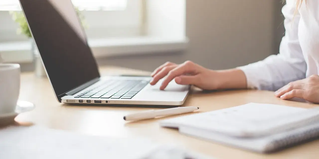 Mano su laptop, penna e quaderno. Ricerca su quanto guadagna un traduttore.