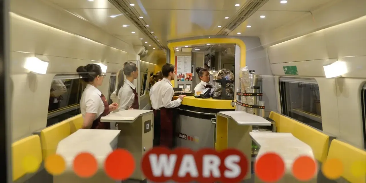 Wnętrze pociągu z personelem obsługującym bar. Widoczny napis "WARS".