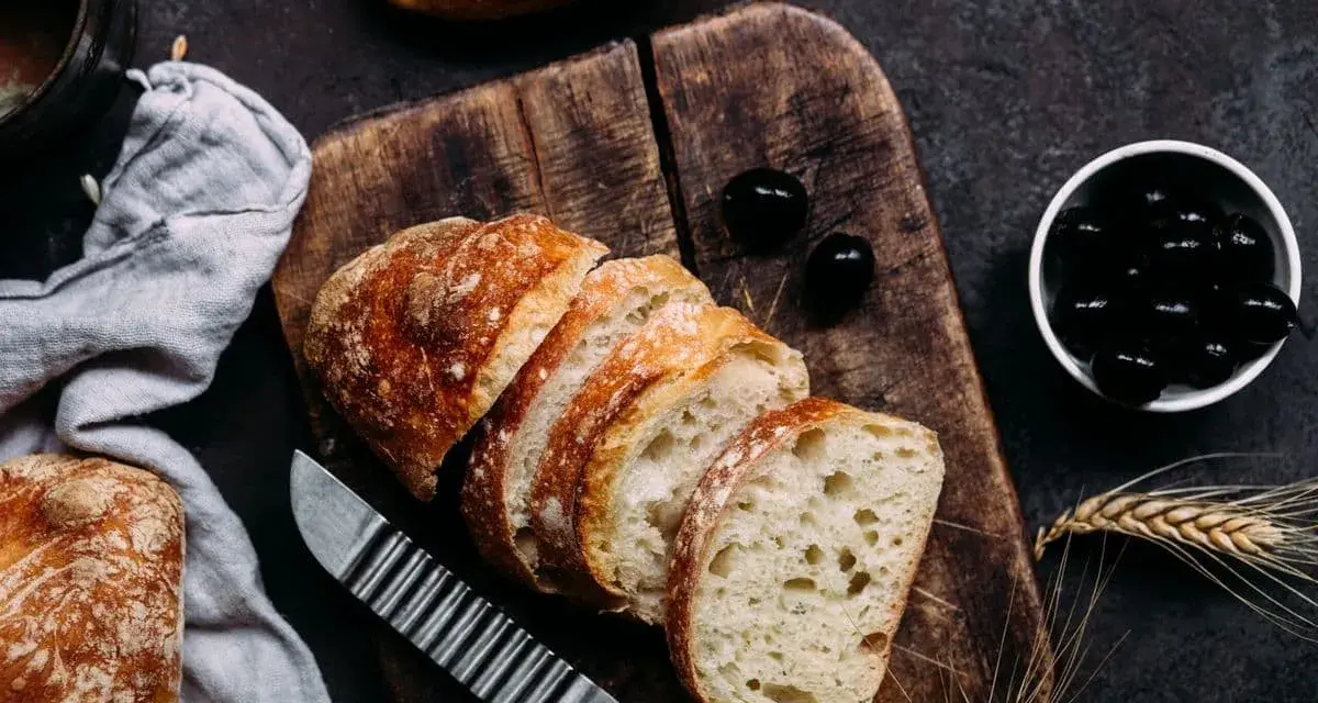 Frisches Brot, aufgeschnitten auf einem Holzbrett, daneben Oliven. Perfekt für den Gasgrill bei richtiger Temperatur.