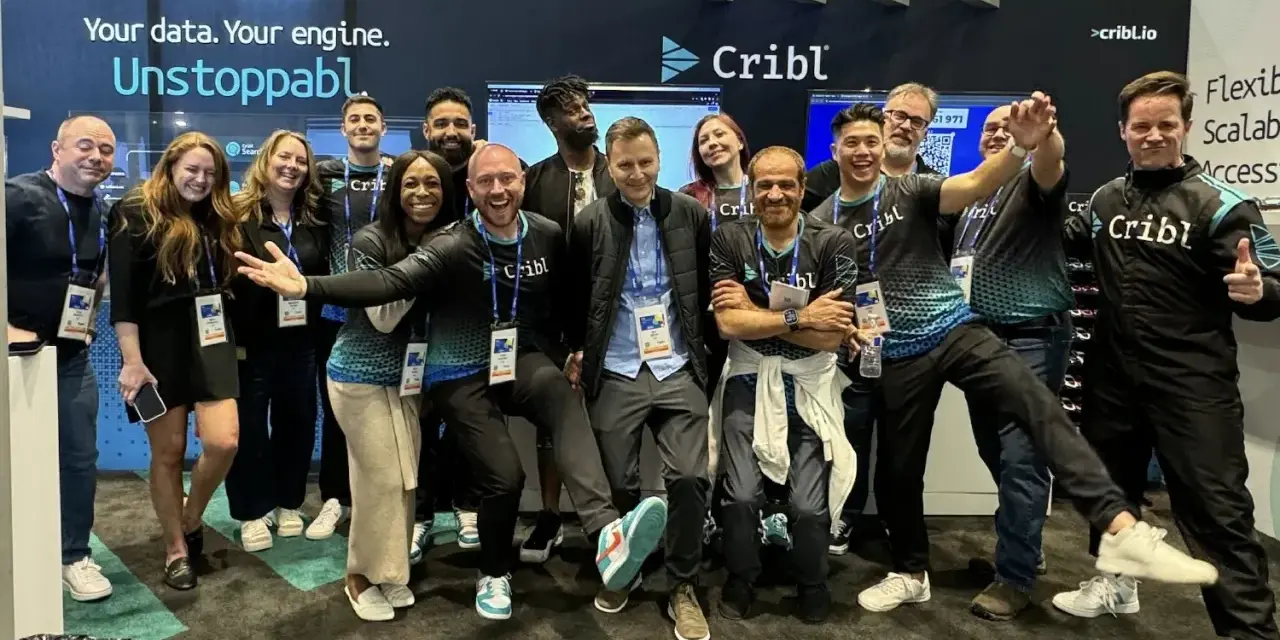 A lively group of Cribl customers and staff pose for a photo at a trade show, all smiles and team spirit.