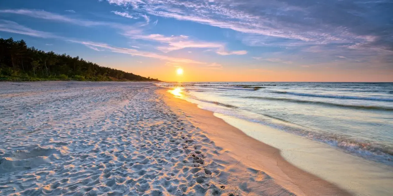 Zachód słońca nad morzem, piaszczysta plaża z ludzkimi śladami, las w tle. Idealne, fajne miejsce nad morzem dla dwojga.